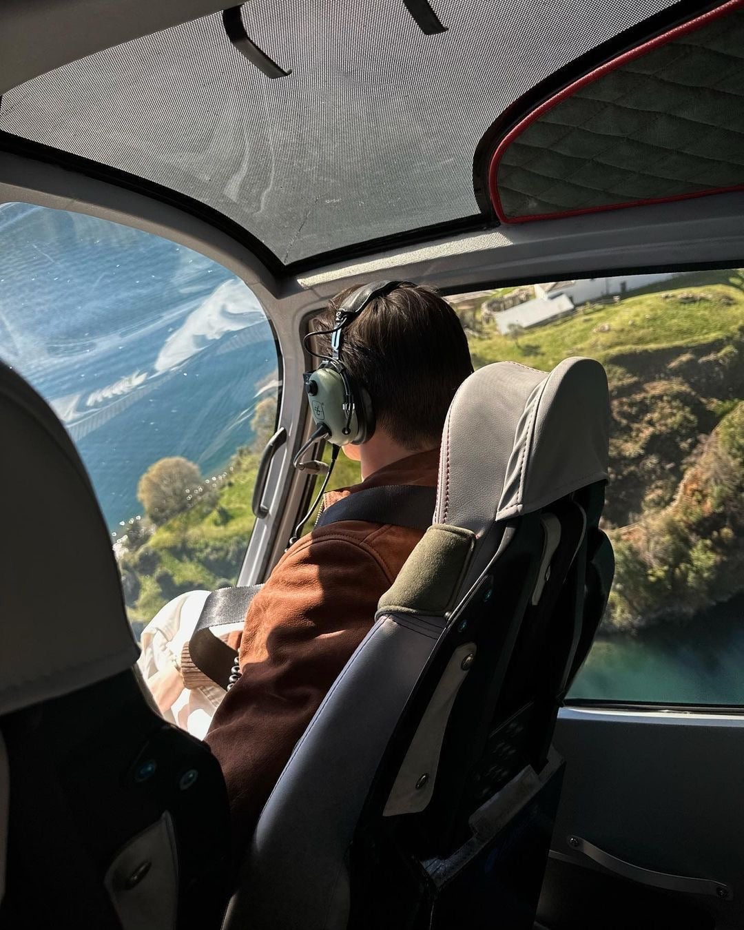 Vista dalla cabina di un elicottero, con un passeggero e il paesaggio oltre il finestrino